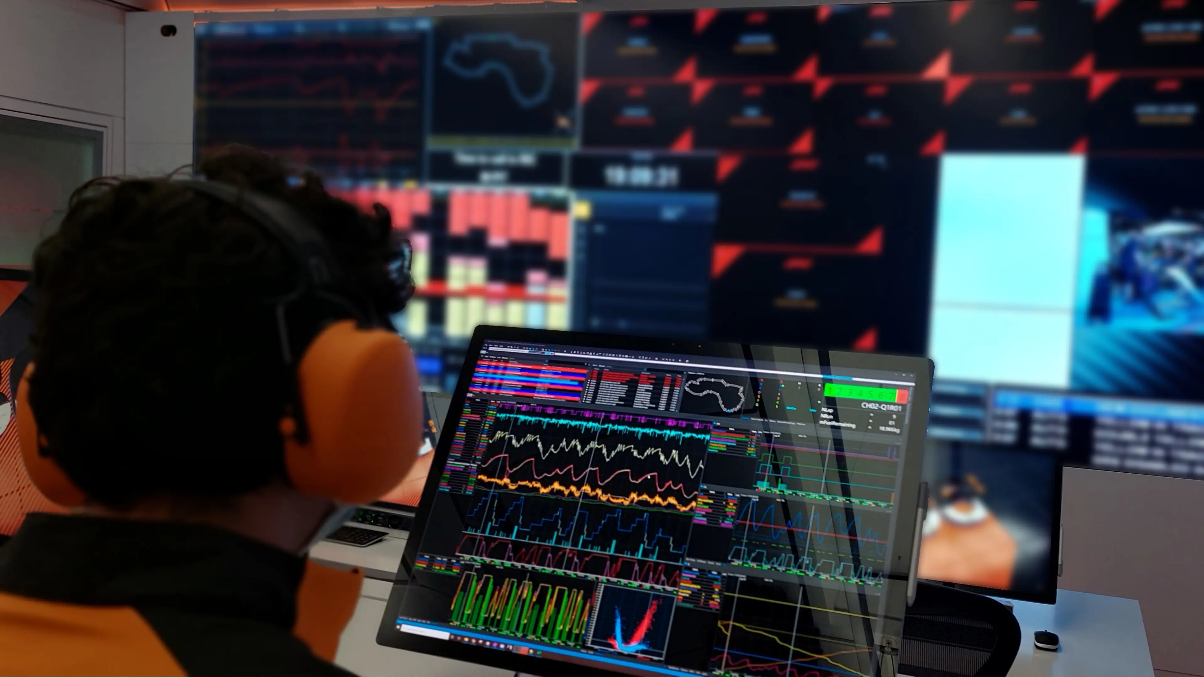 Two people, one with a shirt branded with “Motion Applied” are standing in front of laptops and monitors displaying technical data in a control room setting.