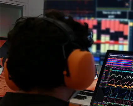 Two people, one with a shirt branded with “Motion Applied” are standing in front of laptops and monitors displaying technical data in a control room setting.