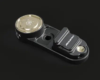 A small black automotive sensor with a circular metallic component on one end and a rectangular section labeled on the other, placed on a dark surface.