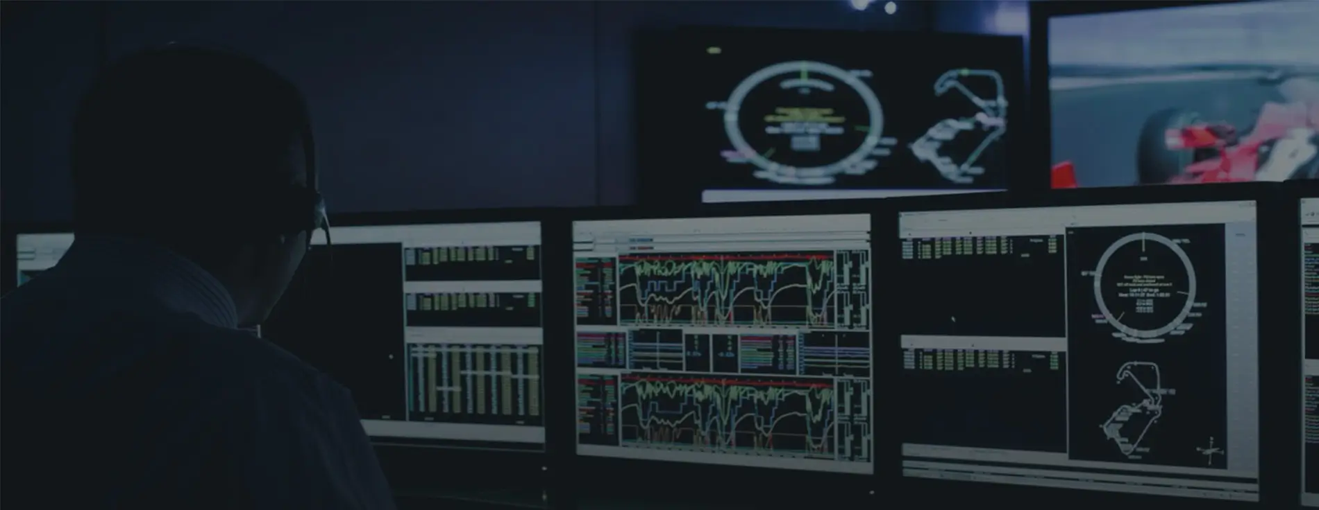 A race engineer uses ATLAS in a race team strategy room. Multiple screens show race telemetry and other information, and another screen shows a red race car is shown on track.