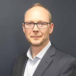 Matt Christie, Director, Business Technology, wearing a dark gray suit jacket over a white collared shirt, posed against a plain dark gray background.