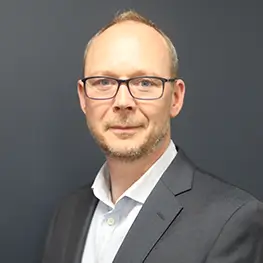Matt Christie, Director, Business Technology, wearing a dark gray suit jacket over a white collared shirt, posed against a plain dark gray background.