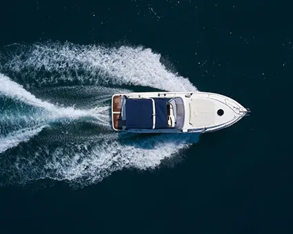 Aerial view of a white motorboat cruising on deep blue water, leaving two curved trails of white wake behind.   Image depicting the Marine market
