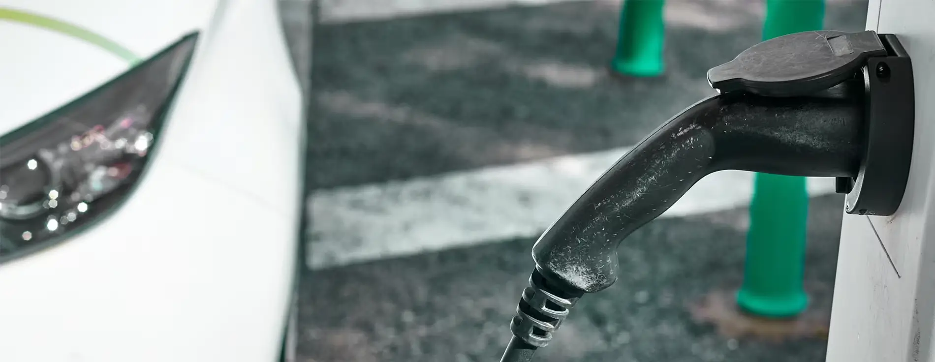 Close‑up of an electric vehicle charging connector plugged into a charging unit, shown against an outdoor parking surface with AMPEX branding visible.