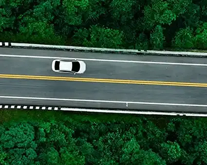 Aerial view of a winding two‑lane road cutting through dense green forest, with a single car driving along the curve.