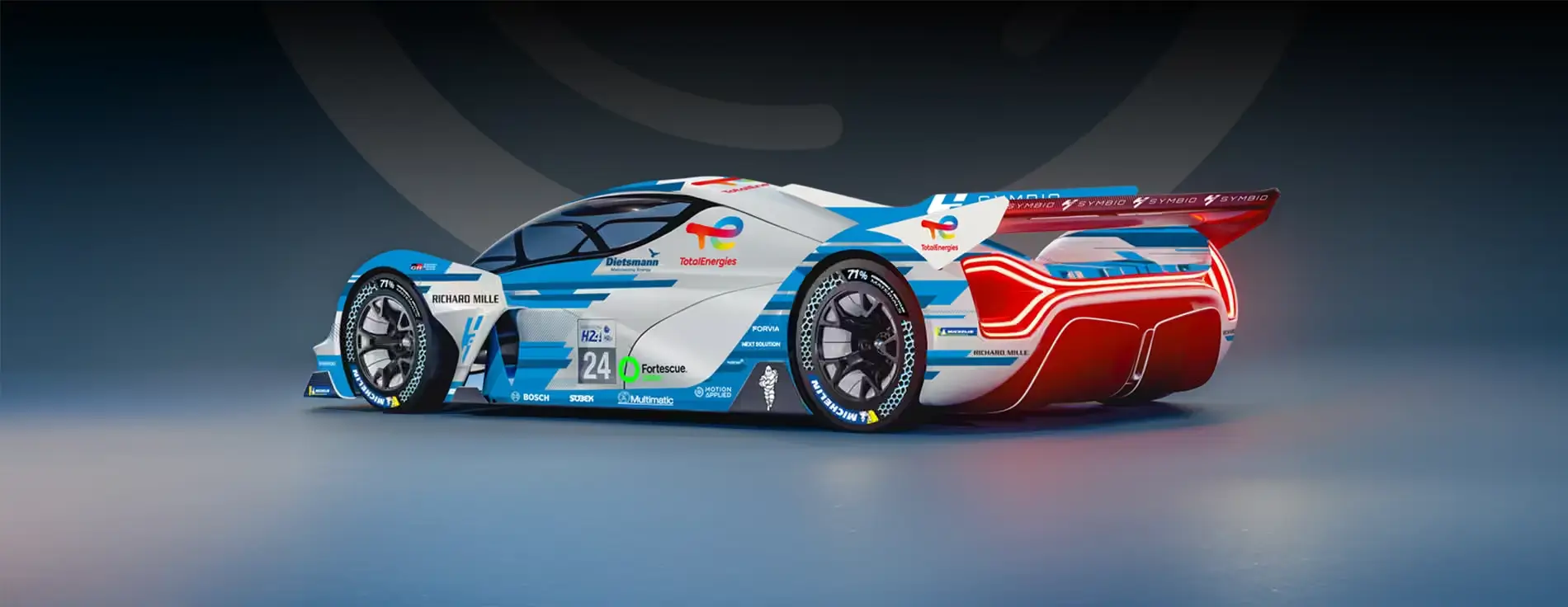 Side‑rear view of a futuristic endurance race car with blue, white, and red livery, aerodynamic bodywork, large rear wing, and sponsor logos, displayed in a studio setting on a neutral background.