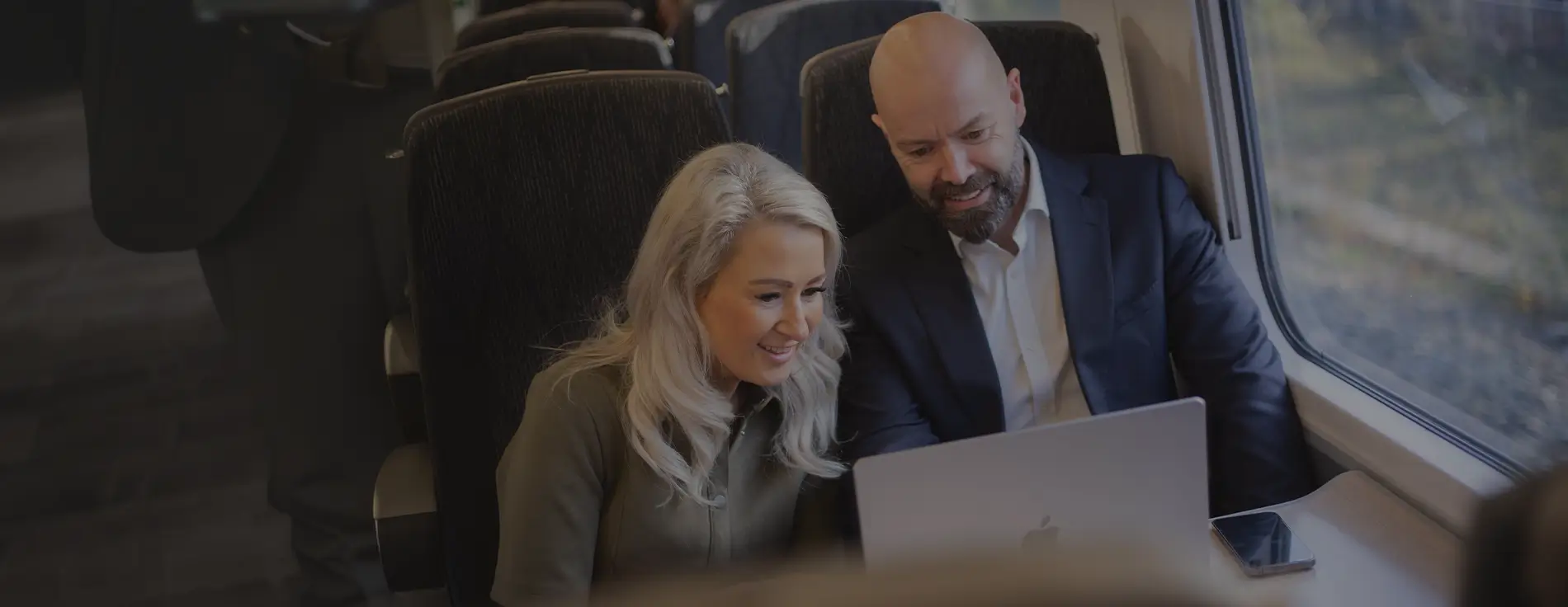 Two smiling people looking at a laptop, on board a passenger train