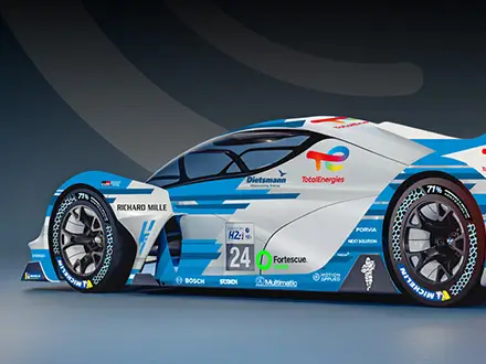 Side‑rear view of a futuristic endurance race car with blue, white, and red livery, aerodynamic bodywork, large rear wing, and sponsor logos, displayed in a studio setting on a neutral background.
