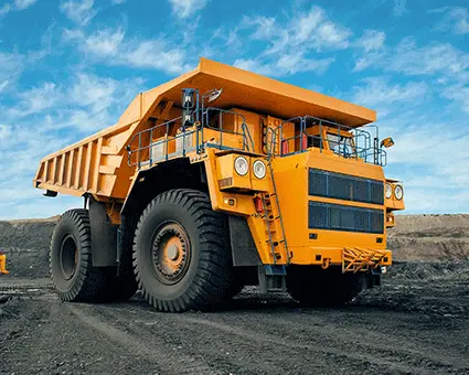 Large yellow mining haul truck driving on a dirt road in an open‑pit mine, with another haul truck visible in the background under a blue sky.